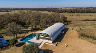 Aerial view of S-Model house with recessed white end wall and large windows, several side windows, and large L-shaped pool