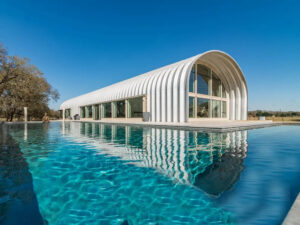 S-Model house with recessed white end wall and large windows, several side windows, and large L-shaped pool in front