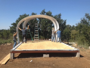 Four people placing steel arches on a raised wooden platform.