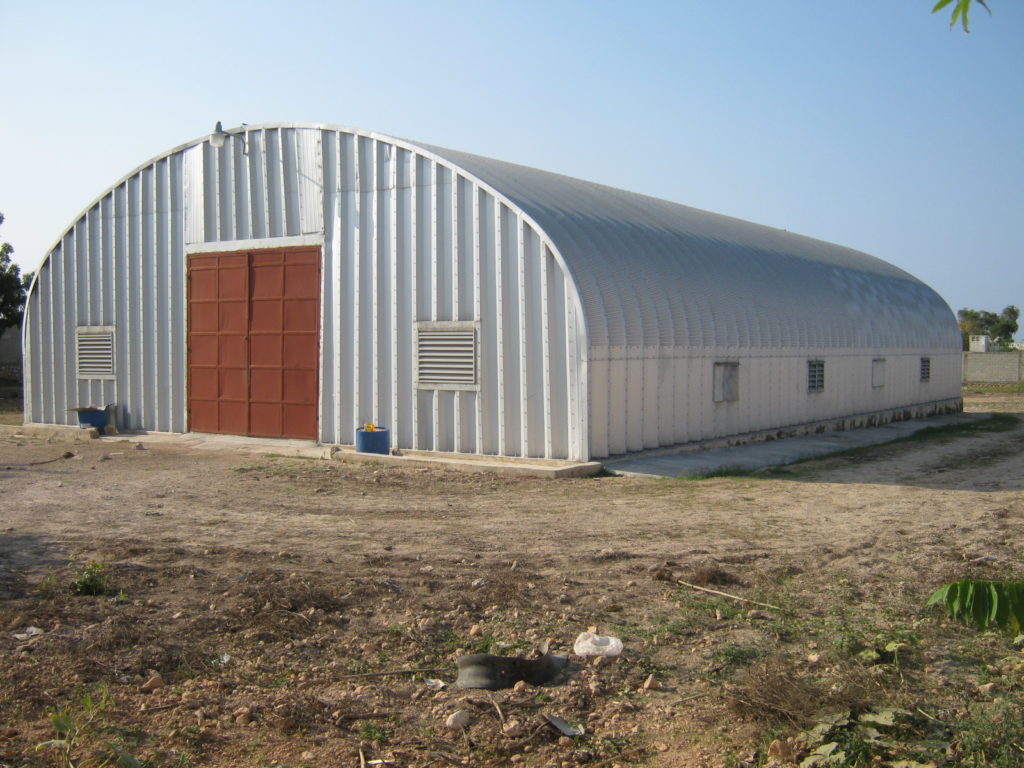 A-model steel shelter with metal endwall, large brown entrance doors, ventalation units on front face and sides of structure.