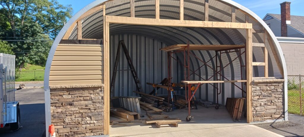 Mid-assembly of Quonset garage, back metal endwall, custom front endwall of wood and stone