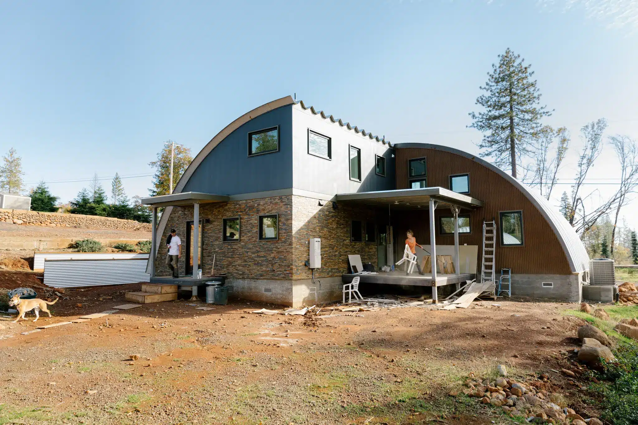 two people and dog on the exterior of a custom-built Quonset hut home