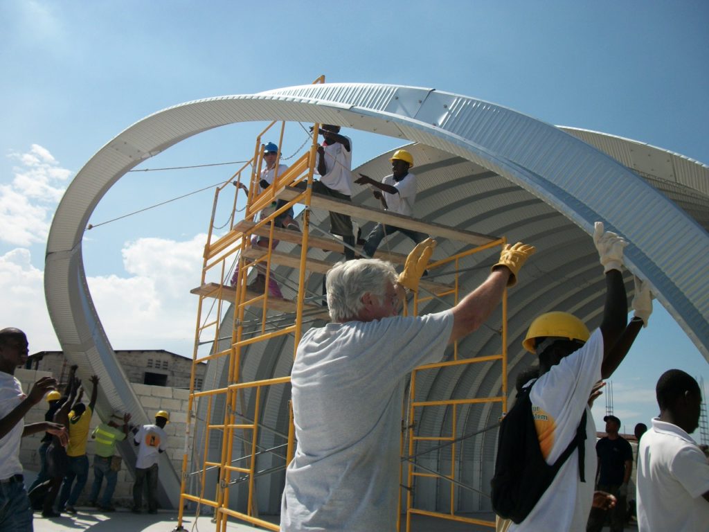 Team lifting metal arch into position on an emergency response shelter.