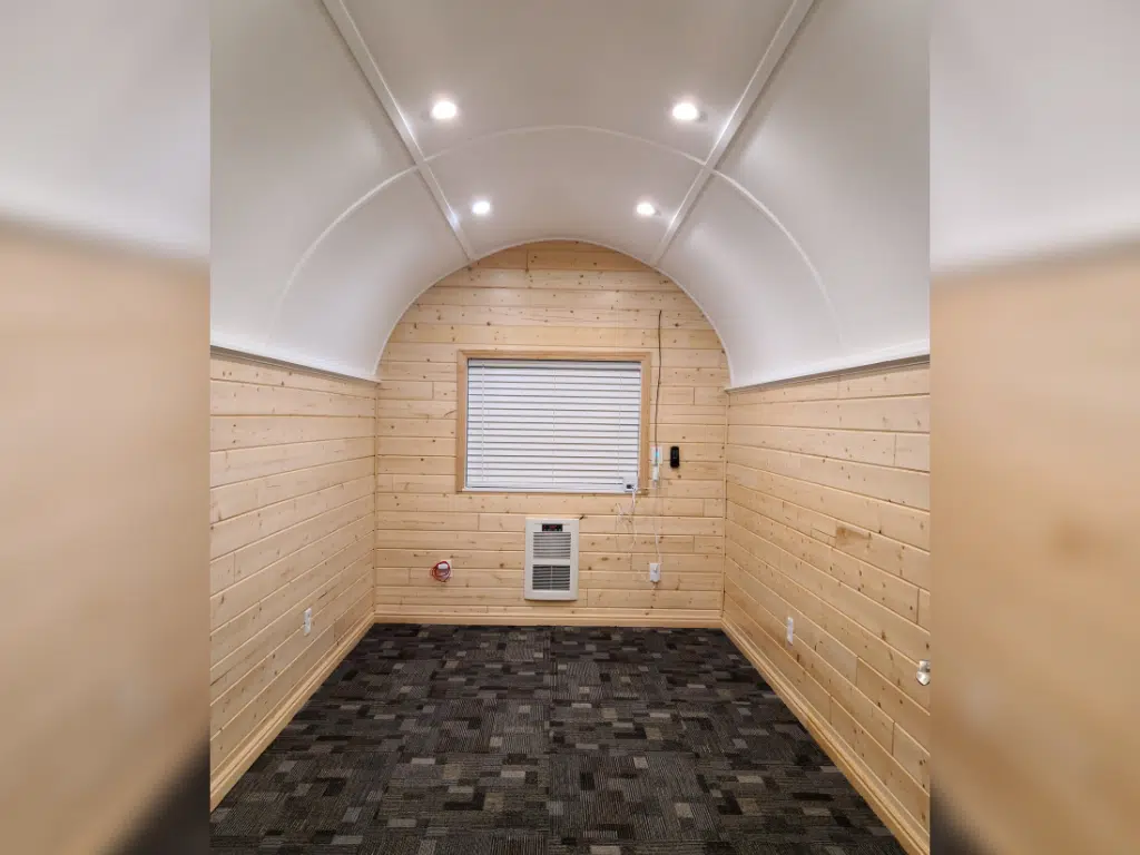 Inside tiny Quonset shed, wood plank walls, covered white ceiling with lights, carpet flooring.