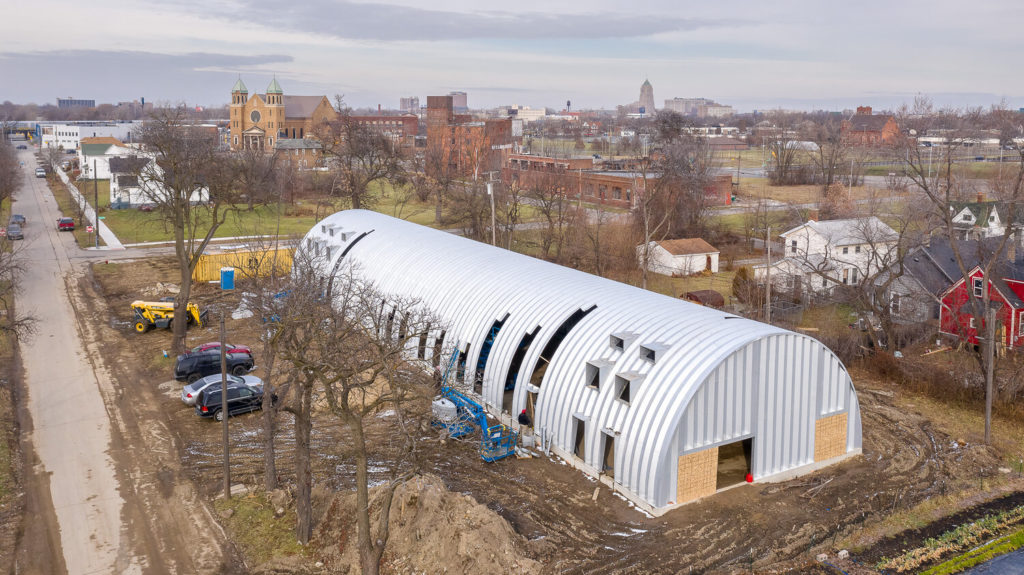 Large Quonset housing project under construction in Detroit, steel endwall, openings in side arches for windows and separate entrances.