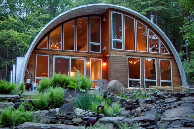 Q-model Quonset home in the forest with custom endwall made of wood and large windows.