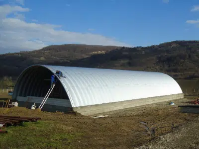 Large Q-model Quonset on raised foundation, man working on roof.