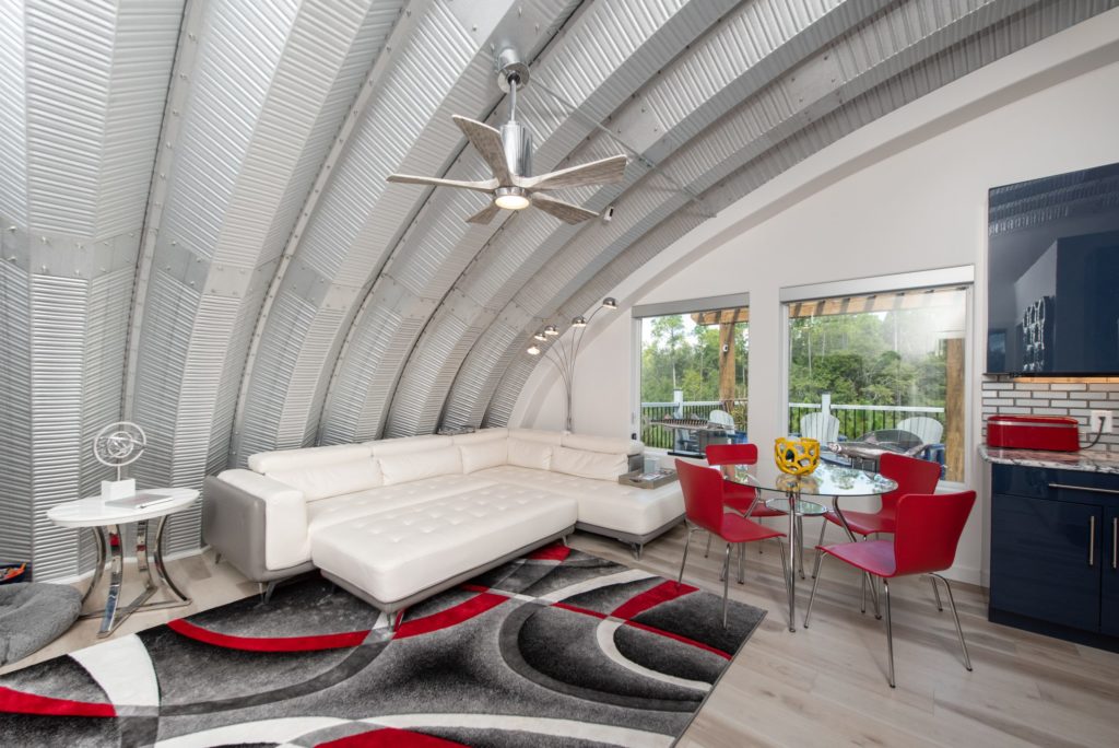 Inside of Quonset home living and dining area, white couch, red chairs and round glass table