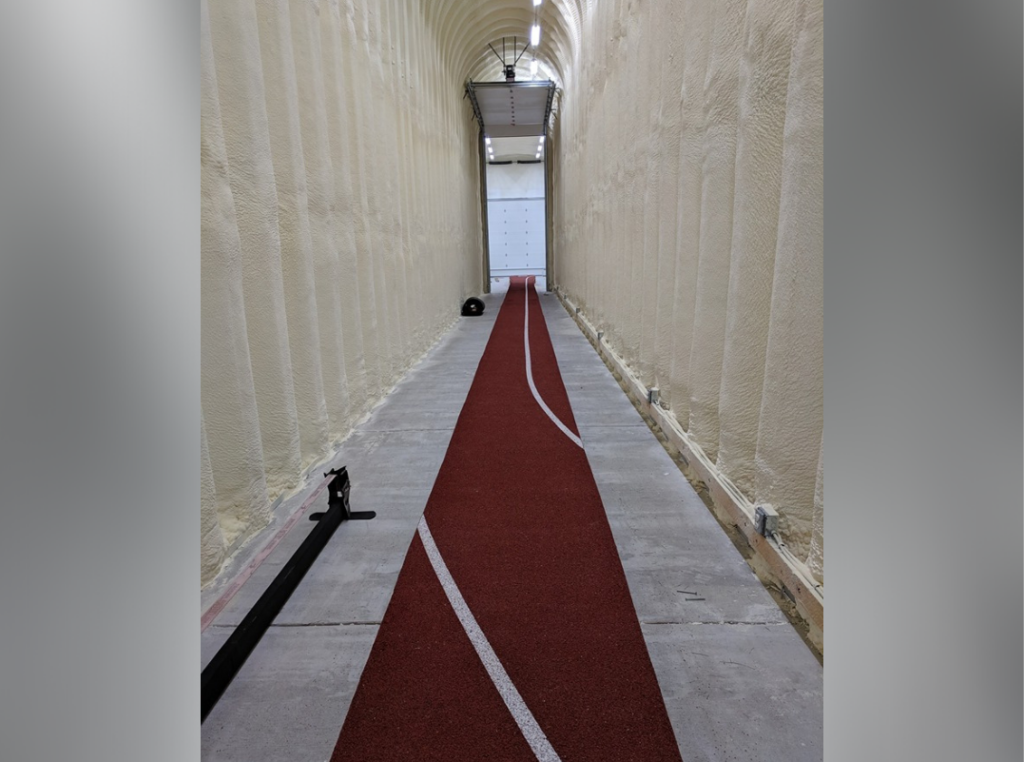 Inside a custom built Quonset hut: small hallway connecting two buildings with a red runway for pole vaulting.