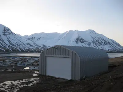 A-model Quonset hut with metal endwall and white rolling door, snowy mountain landscape.